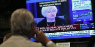 Ein Börsianer schaut auf einen Bildschirm, auf dem eine Rede von Janet Yellen übertragen wird.