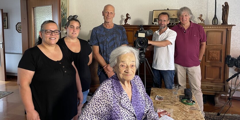 Fatima Adam steht mit dem Team des Saar­ländischen Rundfunks in einem Wohnzimmer.