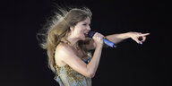 Taylor Swift mit wehendem Haar zeigt ins Publikum und singt