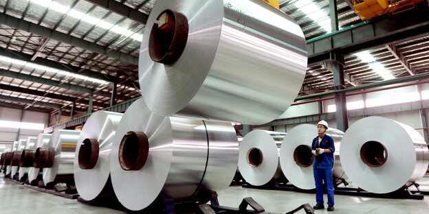 Riesige Aluminiumrollen in einer Halle mit einzelnem Arbeiter