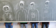 Vier Schüler stehen nebeneinander hinter einer Klassentafel. Ihre versteckten Oberkörper sind auf die Tafel gezeichnet.