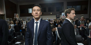 TikTok-CEO Shou Zi Chew und Meta-CEO Mark Zuckerberg, hinter ihnen halten Menschen Fotos von Angehörigen in die Höhe