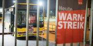 Ein Schild mit der Aufschrift "Warnstreik" prangt an einem Gitter. Dahinter steht ein Bus.