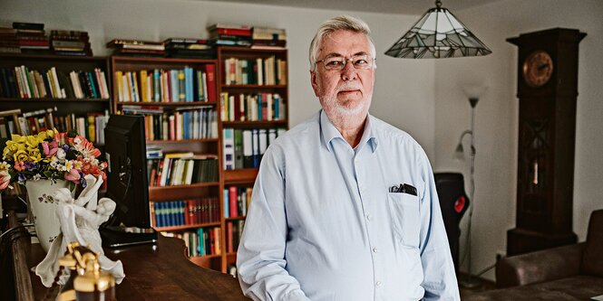 Ein Mann im hellblauen Hemd steht vor einer Bücherwand