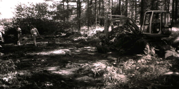 Ein Bagger in einem Wald vor der Grabungsstätte (schwarz-weiß)