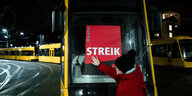 Frau klebt "Streik"-Poster ans Frontfenster einer Tram