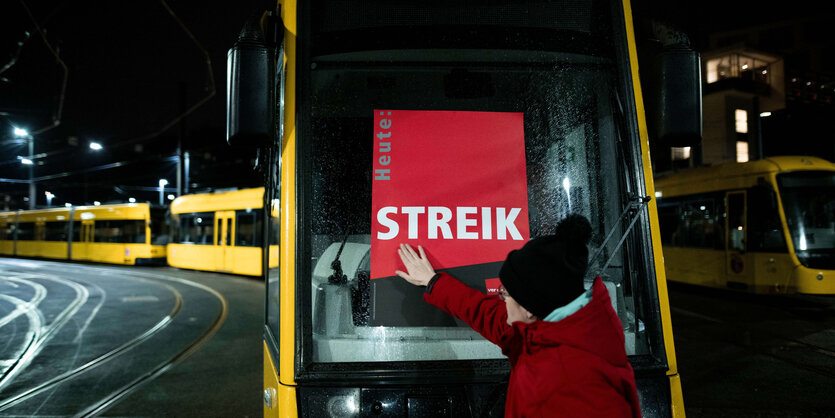 Frau klebt "Streik"-Poster ans Frontfenster einer Tram