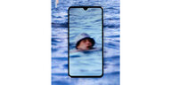 Ein junge mit blauem Hut schwimmt im Wasser, durch ein Smartphone wird er herangezoomt