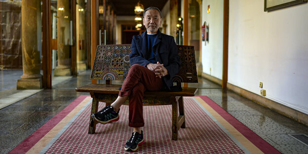 Der japanische Autor Haruki Murakami sitzt auf einem verzierten Holzsessel in einem Museum