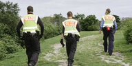 Drei Polizisten laufen einen Parkweg entlang