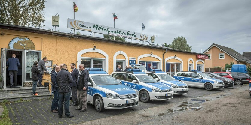 Restaurant "Mittelpunkt der Erde" in einem flachen Gebäude, davor Polizisten und Polizeiautos