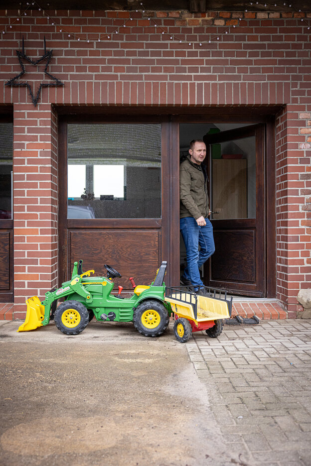 Eine Person steht in einem Hauseingang, davor ein Kindertraktor