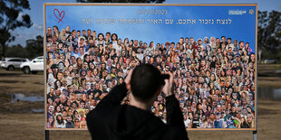 Eine Person vor einem Plakat, auf dem Portraits vieler Leute abgebildet sind