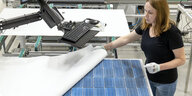 eine Frau mit weißen Handschuhen hebt die Bedeckung von blauen Solarzellen ab