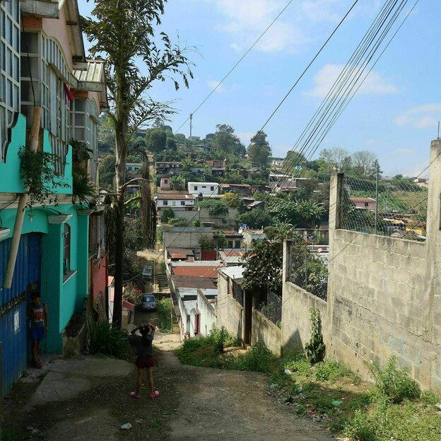 Blick in den Stadtteil rund um die Schule der Hoffnung, eine unverputzte Mauer steht an einem steilen, ungepflasterten Weg, gegnüber bunt angemalte Häuser