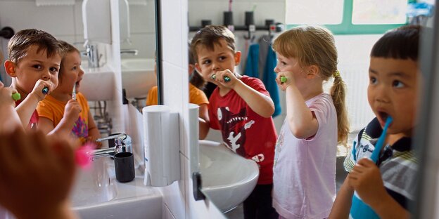 Kinder stehen vor einem Spiegel und putzen sich die Zähne