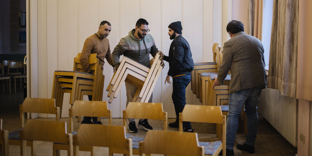 Menschen tragen Stühle und räumen in einem kirchlichen Gemeindehaus auf