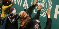 Mehrer protestierende Frauen schlagen mit Händen an eine Wand, auf der das Logo der UNRWA abgebildet ist