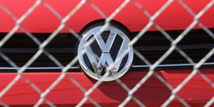 Das Volkswagen-Logo auf einem roten Auto hinter einem Zaun.