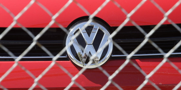 Das Volkswagen-Logo auf einem roten Auto hinter einem Zaun.