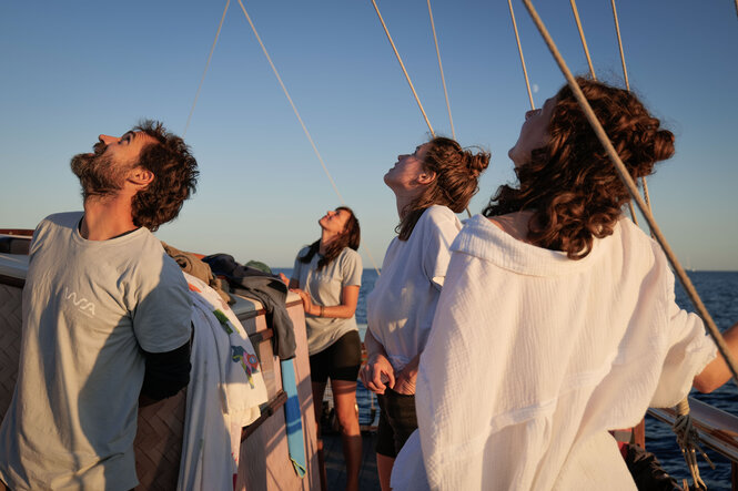 Eine Gruppe Menschen schaut auf einem Boot richtung Himmel.