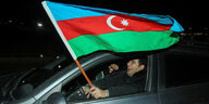 Ein Unterstützer von Amtsinhaber Ilham Alijew sitzt lachend im Auto und hält freudig eine Flagge Aserbeidschans aus dem Fenster