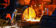 Ein Stahlarbeiter im Schutzanzug entnimmt eine 1500 Grad heisse Roheisenprobe beim Abstich am Hochofen.