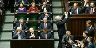 Polnisches Parlament, auf der linken Seite sitzen die Abgeordneten der PIS, rechts daneben Donald Tusk , der von einem Mann mit Smartphone fotografiert wird, im Vordergrund wird an einem Tisch verhandelt