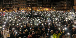 In Frankfurt am Main halten hunderte Demonstrierende leuchtende Handys in den Abendhimmel.