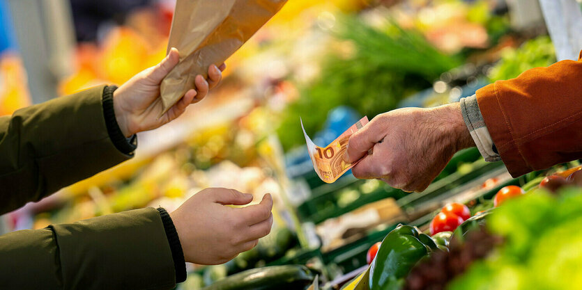 An einem Marktstand wird mit Bargeld eingekauft.