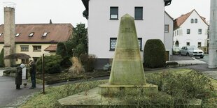 Der Gedenkobelisk mit der Inschrift: Wir gedenken der Opfer des anglo-amerikanischen Bombenterrors, steht mitten im Ort von Nickern zwischen Einfamilienhäuser. Zwei Menschen mit Hund sind auch unterwegs