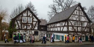 Sorbische Kinder gehen kostümiert an einer Reihe von Fachwerkhäusern vorbei