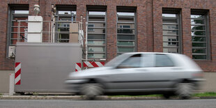 Ein silbernes Auto fährt an einer Messstation für Feinstaub vorbei.