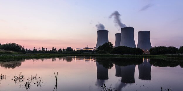 Vier Reaktoren sind im Hintergund vor einem Gewässer zu sehen, vor Sonnenuntergang