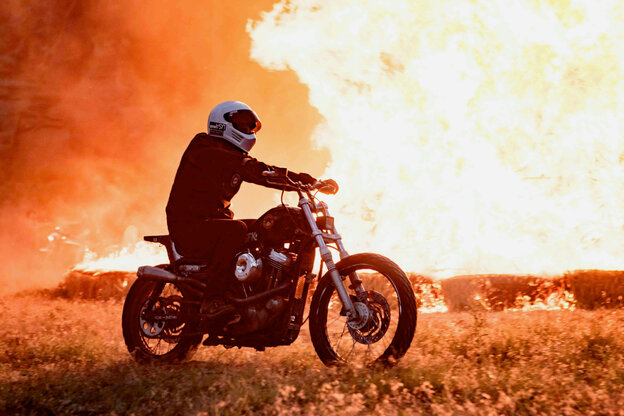 Person auf einem Motorrad im Vordergrund, im Hintergrund ein Feuersturm