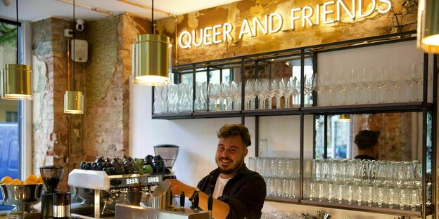 Danjel Zarte steht hinter dem Tresen und zapft ein Bier - über ihm steht in großen hellen Leuchtbuchstaben: queer and friends.