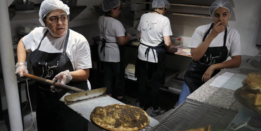 Frauen in einer Bäckerei, eine schiebt eine Man’ousheh auf ein Blech