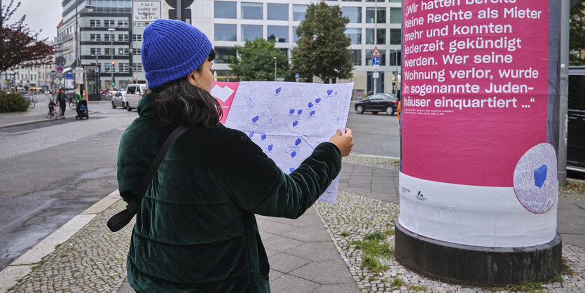 Eine Person steht mit einer Karte in der Hand auf einer Straße. Auf der Straßenkarte sind manche Areale große, dunkelblaue Flecken.