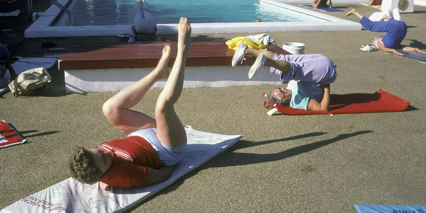 Ältere Menschen liegen auf Turnmatten neben einem Pool und machen Übungen