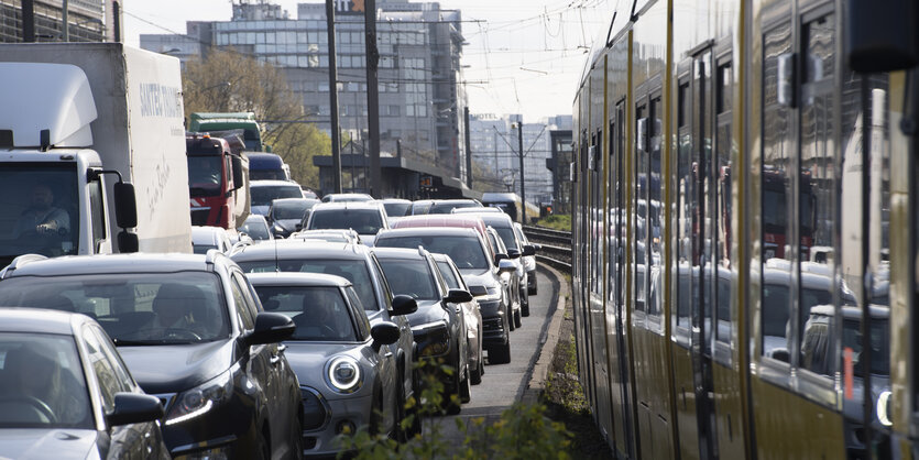 Autos stehen im Stau neben einer gelben Tram der BVG. Im Hintergrund sind Hochhäuser zu sehen.