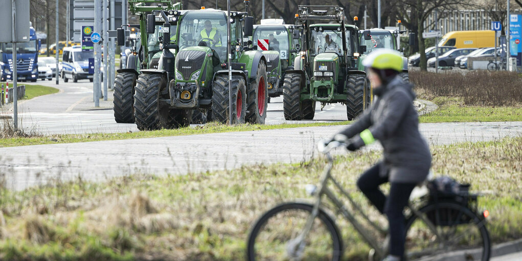 Eine Radfahrerin fährt von rechts nach links, im hinteren Teil des Bildes sieht man Traktoren