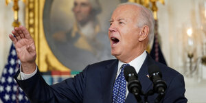 Joe Biden mit erhobener Hand spricht in Mikros.