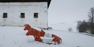 Holzkühe mit Aufschrift "A faire Milch" vor einem Hof im Schnee