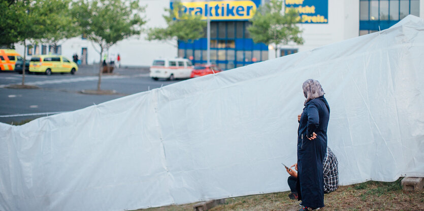 Eine Frau steht an einem Zaun vor einem Baumarkt.