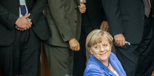 Kanzlerin Merkel lächelt gequält vor lauter Männern