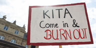 Ein Plakat mit der Aufschrift "Kita Come in & Burn Out" ist während einer Demonstration vor dem baden-württembergischen Finanzministeriium zu sehen.