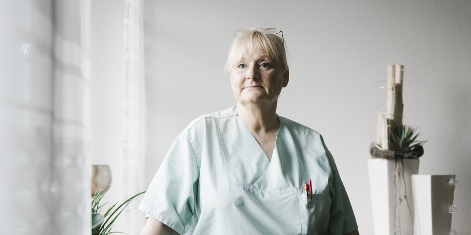 Porträt der Pflegerin Ursula Hoppe-Elsner,sie steht in ihrer Wohnung am Fenster