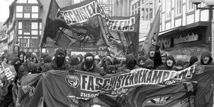 Demonstration mit Transparent. Manche Menschen in den forderen Reihen sind vermummt.