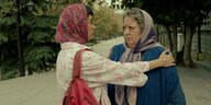 Eine junge Frau spricht mit einer älteren Frau, die skeptisch schaut - beide tragen Kopftücher