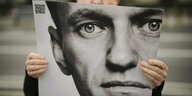Ein Mann hält ein Plakat mit dem Porträt von Alexei Navalny in der Hand, nur seine Finger und die Nasenspitze sind zu sehen.